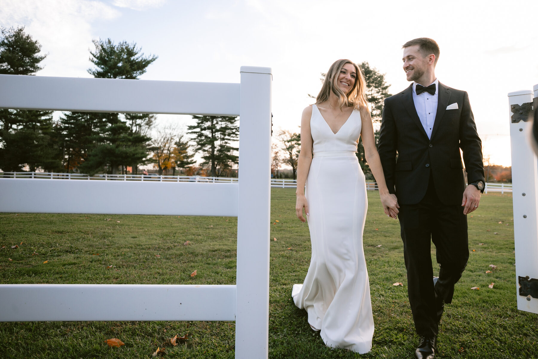 Bride and groom walking along a white country fence